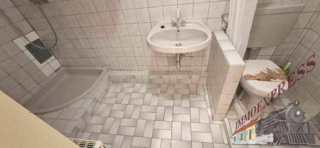 Badezimmer mit weißen Fliesen, Dusche, WC und Waschbecken unter einer Dachschräge.