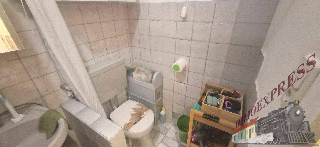 Funktionales Badezimmer mit weißen Fliesen, WC, Waschbecken und Duschbereich.