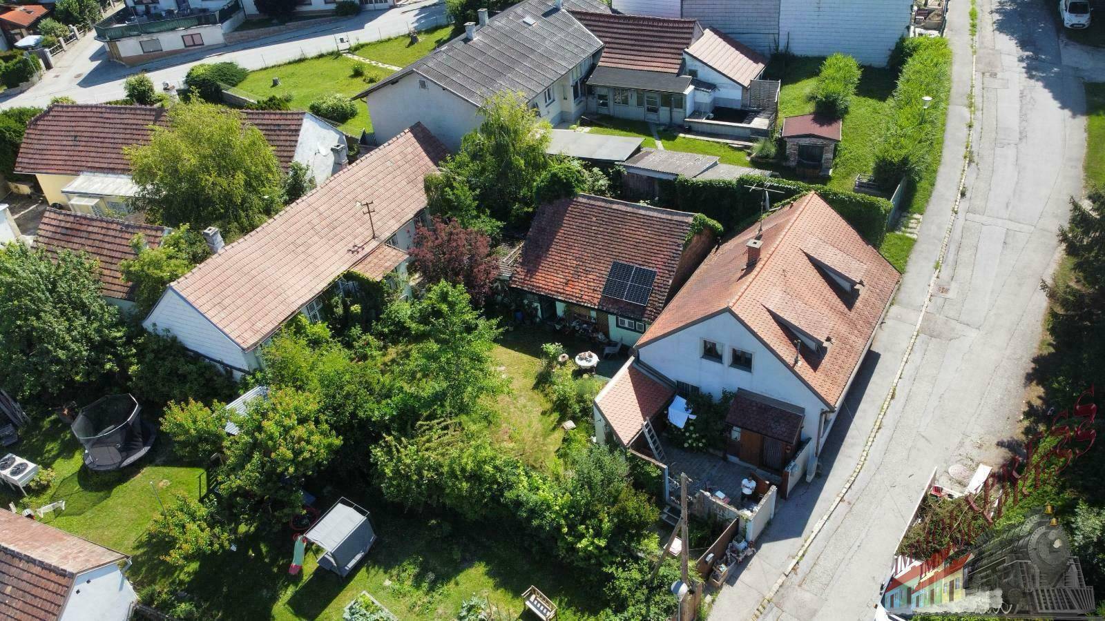 Luftaufnahme einer ländlichen Wohngegend mit mehreren Einfamilienhäusern, Gärten und viel Grün.