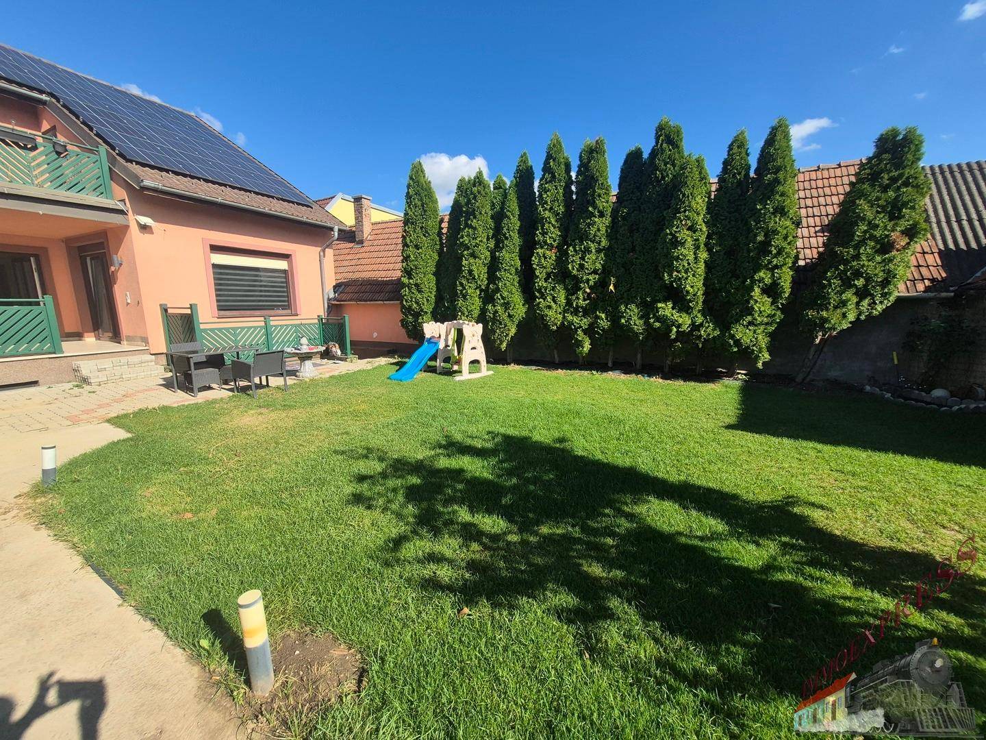 Großer grüner Garten mit Rasenfläche, hohen Bäumen und Kinderspielgerät.