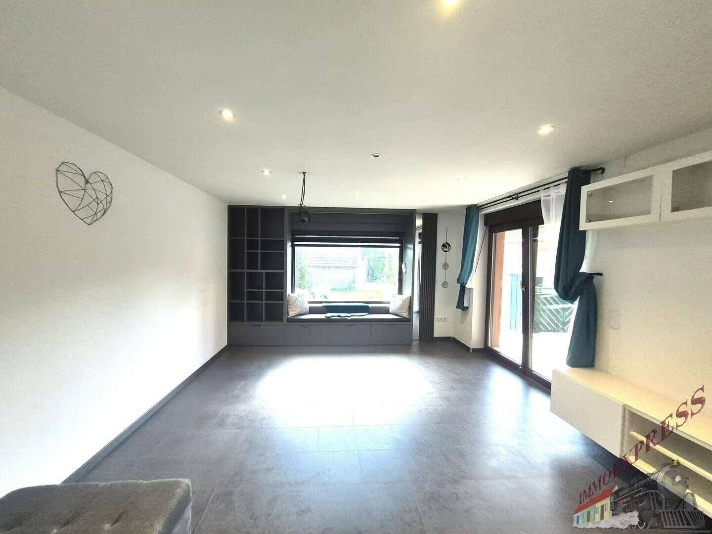 Geräumiges Wohnzimmer mit Fliesenboden, integrierter Fensterbank und Zugang zur Terrasse.