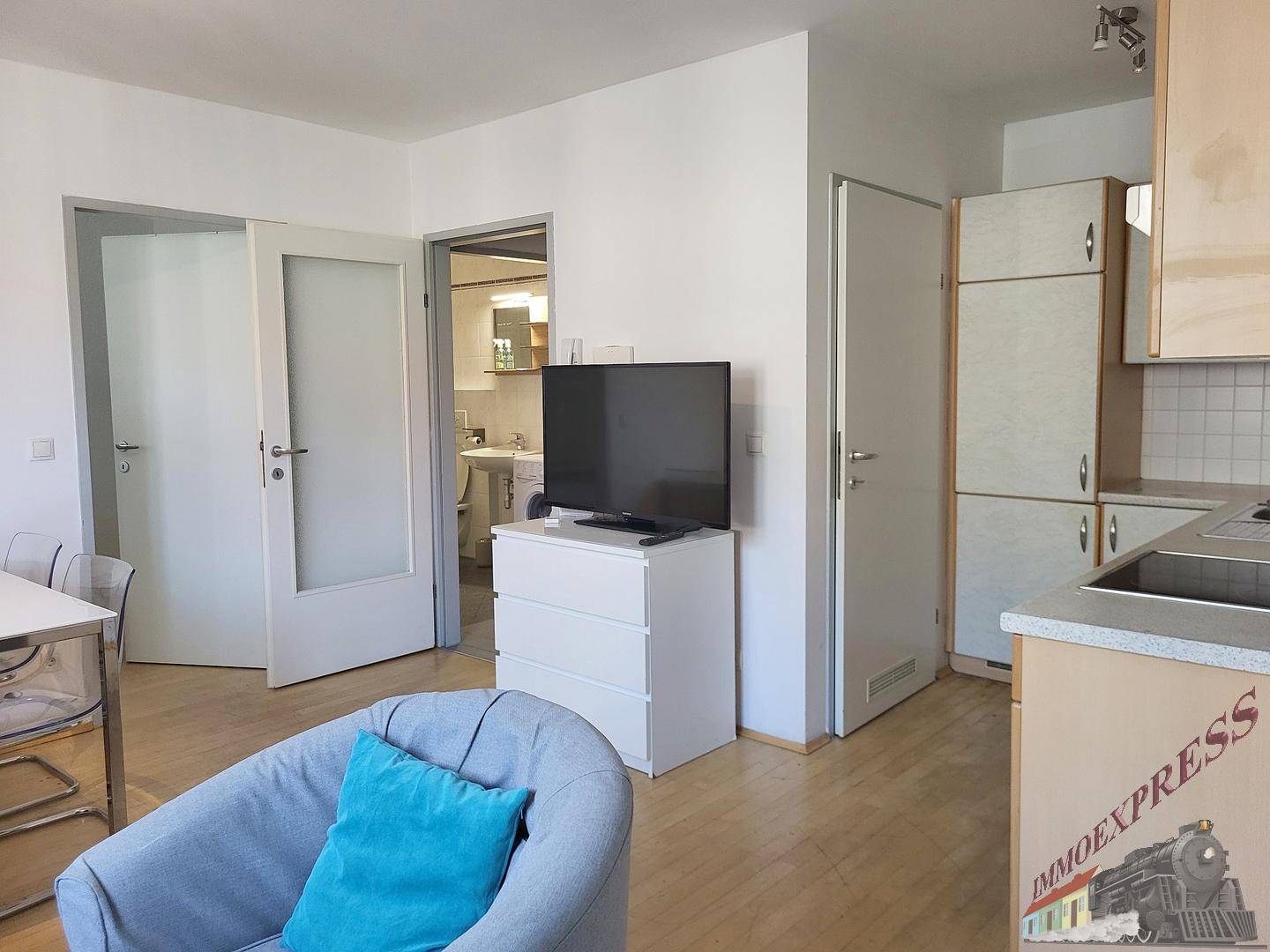 Wohnbereich mit Fernseher und Zugang zur Küche sowie weiteren Räumen.