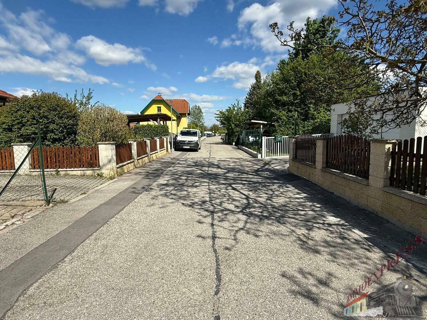 Ruhige Wohnstraße mit Einfamilienhäusern, Zäunen und Bäumen an einem sonnigen Tag.