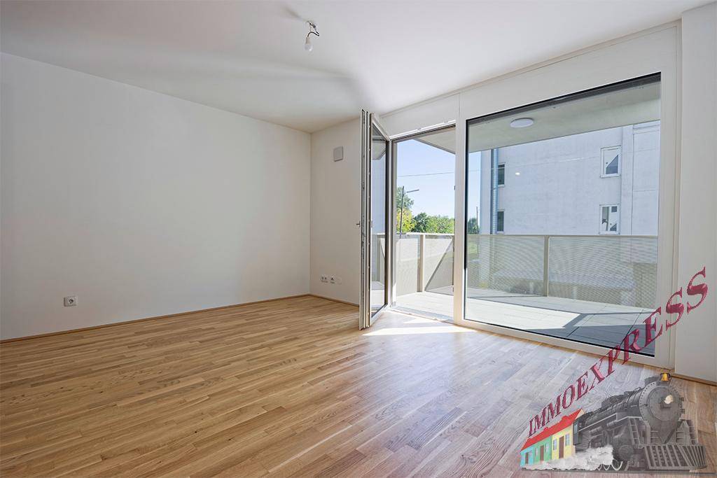 Geräumiges Wohnzimmer mit hellem Parkettboden und großen Fenstern, die auf einen Balkon führen.