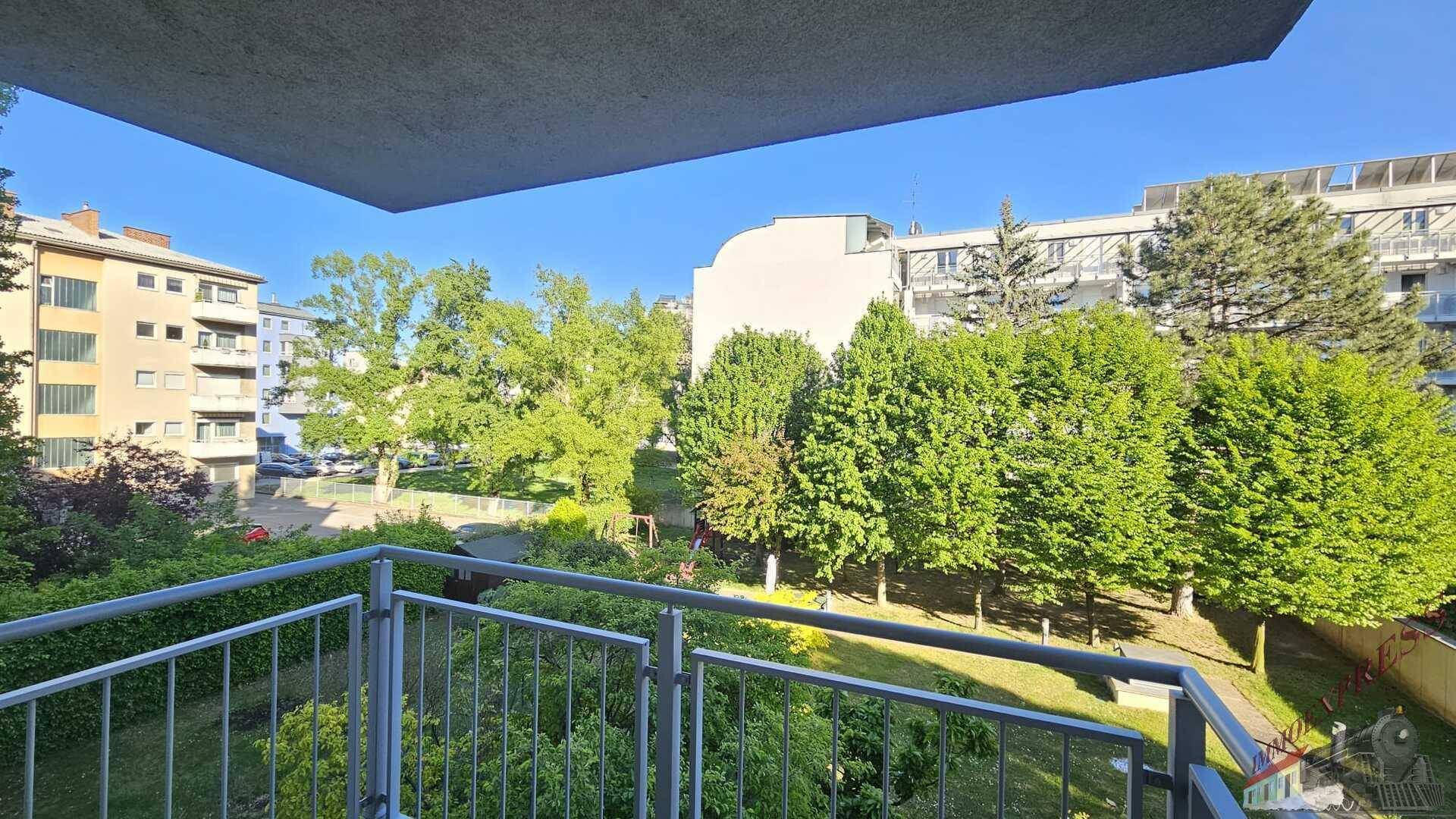 Sonniger Blick vom Balkon auf eine gepflegte Grünfläche und weitere Wohngebäude.