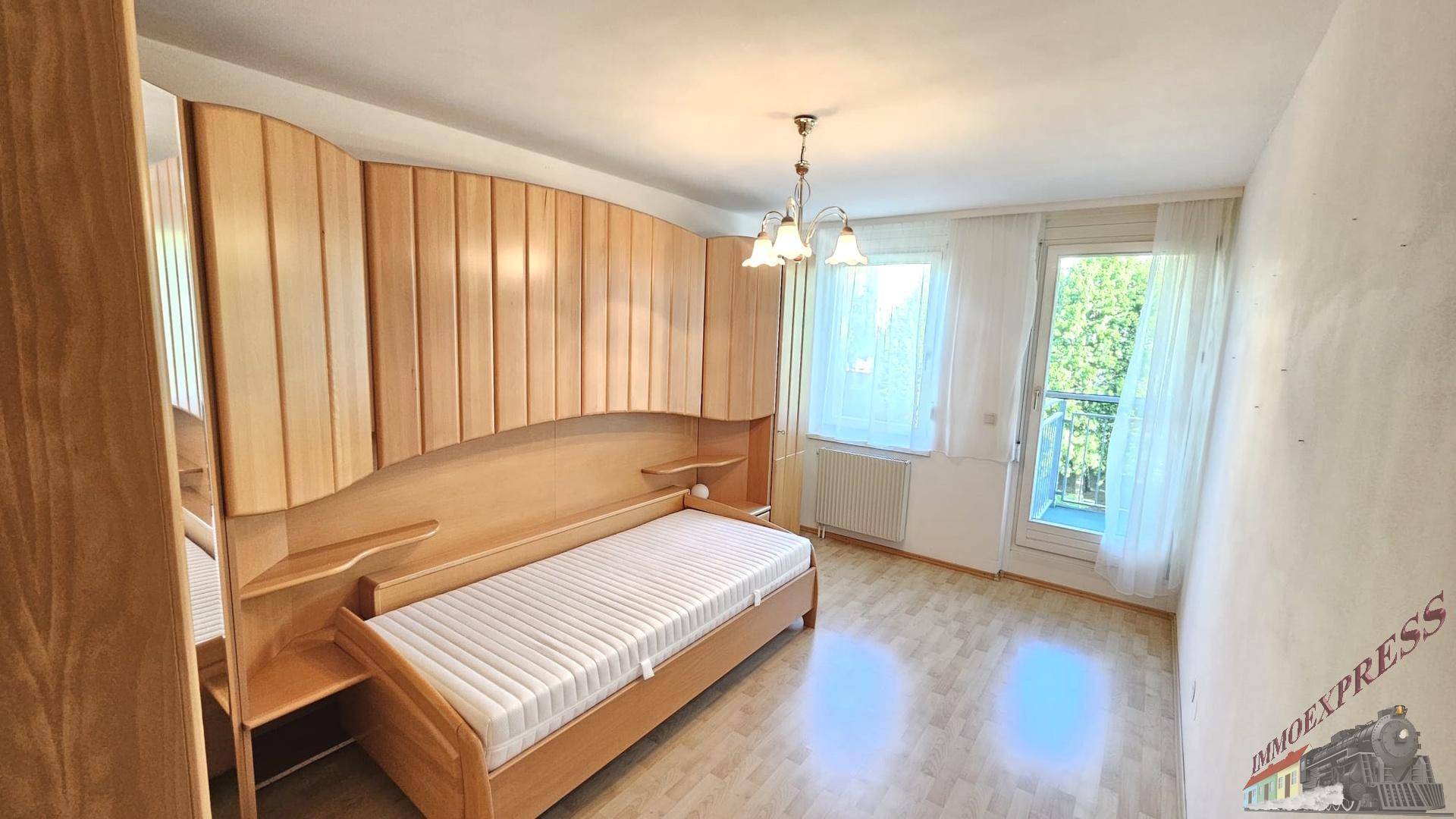 Schlafzimmer mit Einzelbett, integrierten Holzschränken und Zugang zum Balkon.