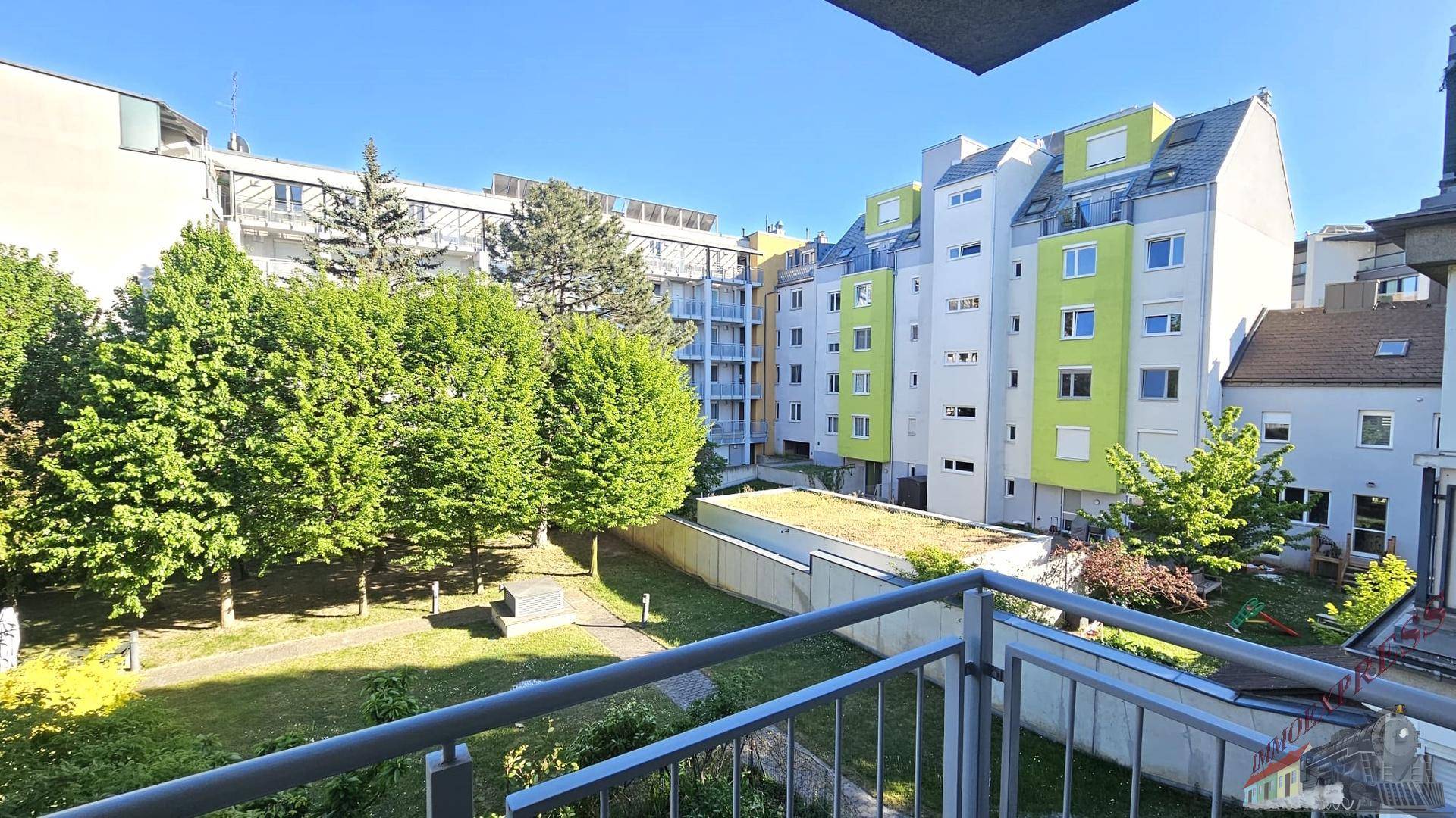 Weiterer Blick vom Balkon auf den begrünten Innenhof und ein modernes Wohngebäude.