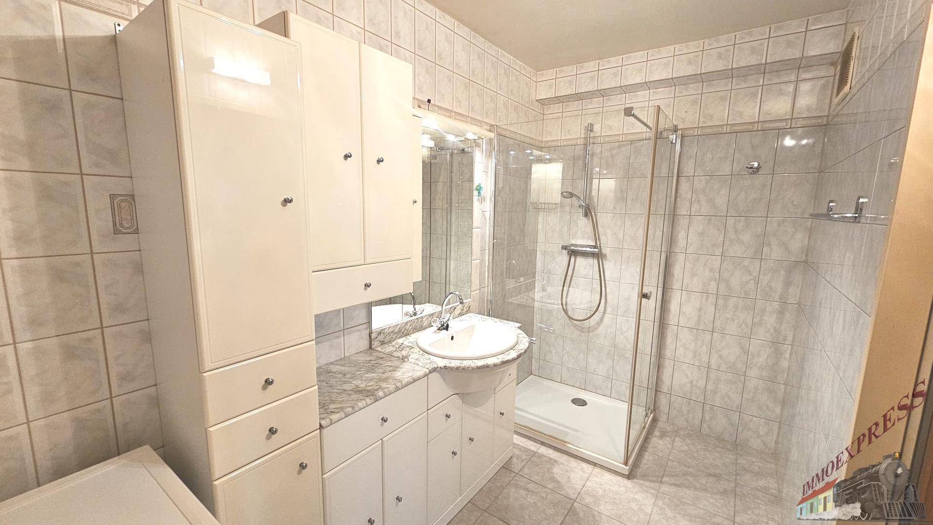 Badezimmer mit hellen Fliesen, Waschtisch und einer modernen Duschkabine.