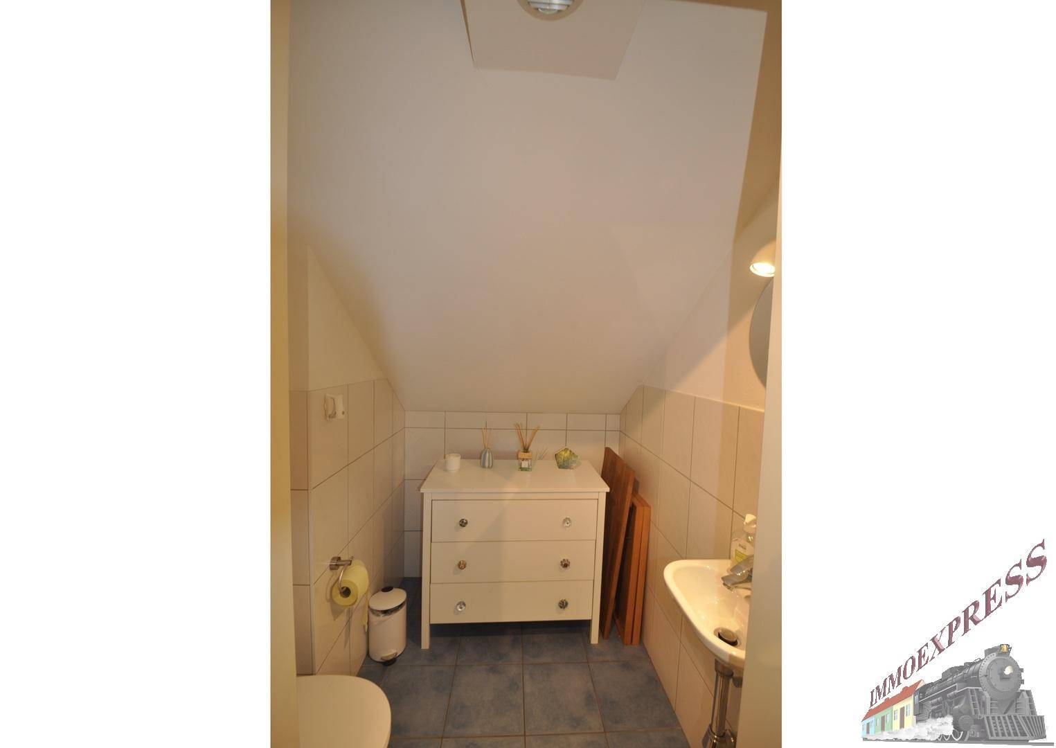 Kleines Gäste-WC mit Waschbecken, Toilette und Fliesenboden unter einer Dachschräge.