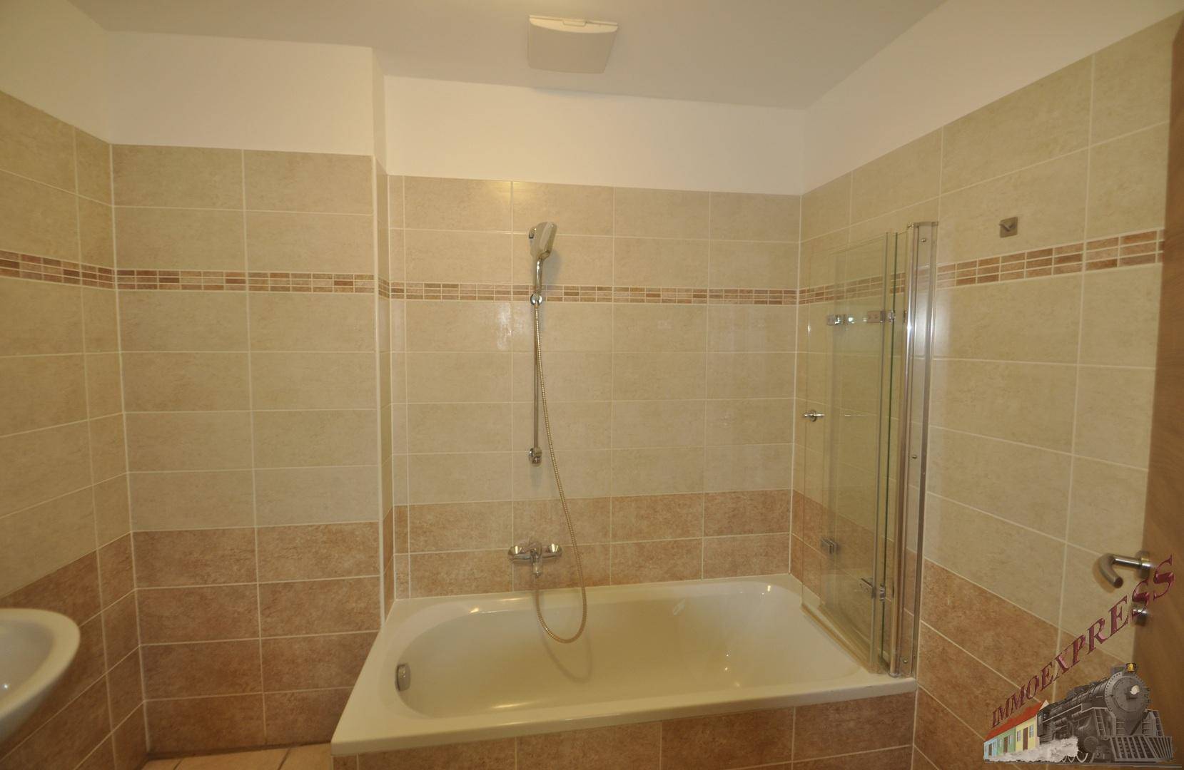 Badezimmer mit beigefarbenen und braunen Fliesen, ausgestattet mit einer Badewanne und Duschabtrennung.