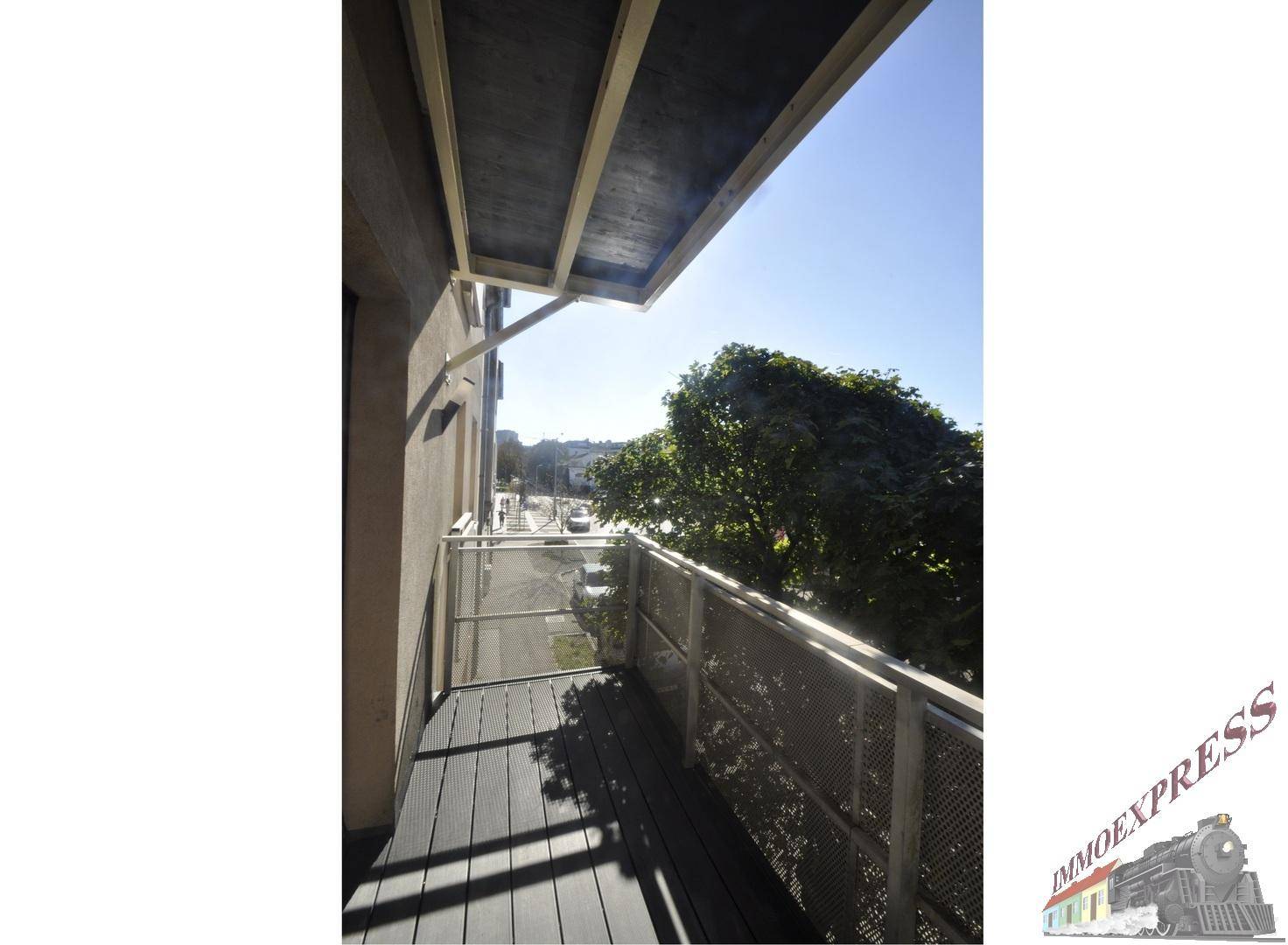 Balkon mit Holzboden und Metallgeländer, bietet einen Blick auf die Straße und Bäume.
