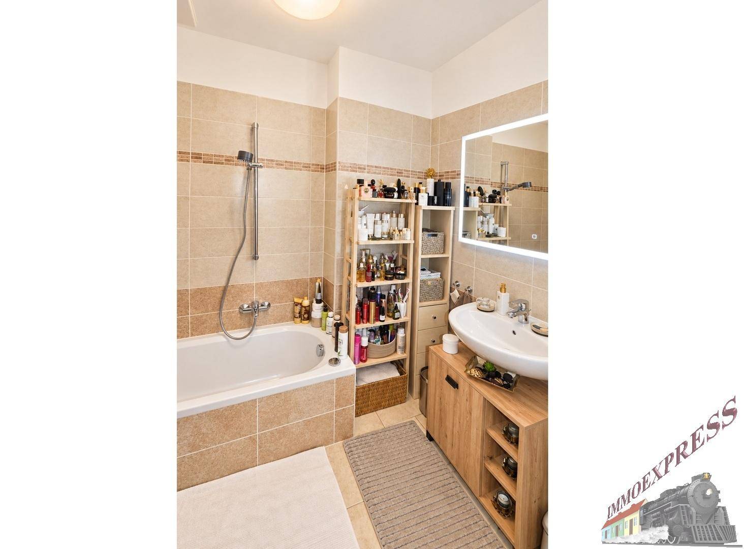 Modernes Badezimmer mit Badewanne, Einzelwaschbecken, beigefarbenen Fliesen und beleuchtetem Spiegel.