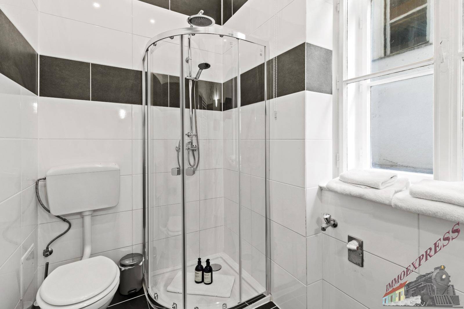 Modern gefliestes Badezimmer mit Duschkabine, Toilette und Fenster für angenehmes Tageslicht.
