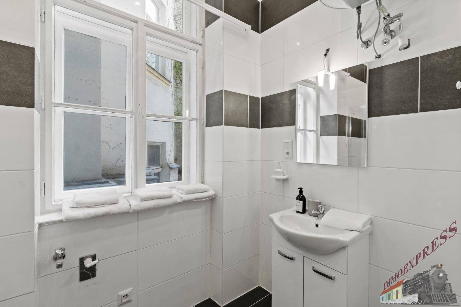 Helles Badezimmer mit Waschbecken, Spiegelschrank und großem Fenster, das viel Licht hereinlässt.
