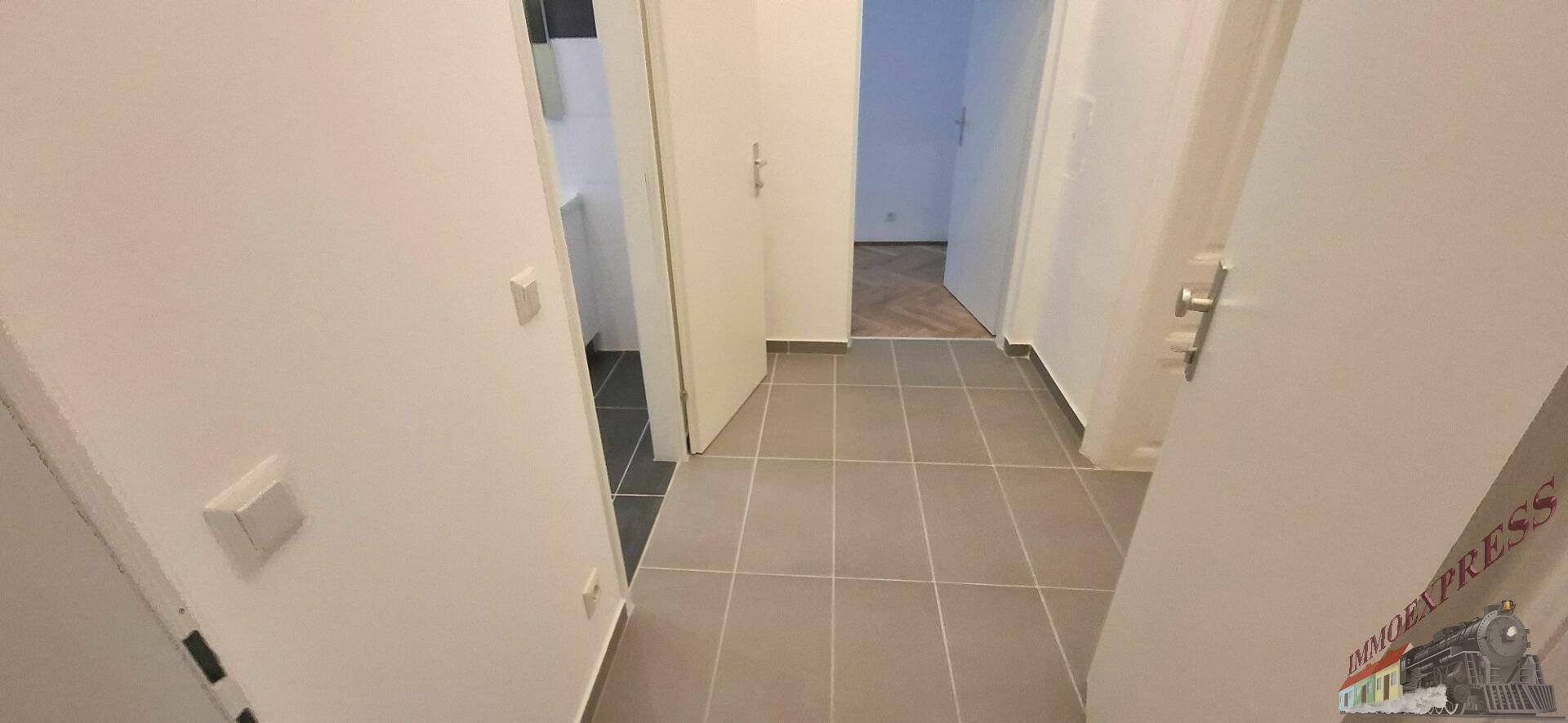 Heller Flur mit modernen Fliesen und mehreren Türen, die zu angrenzenden Räumen führen.