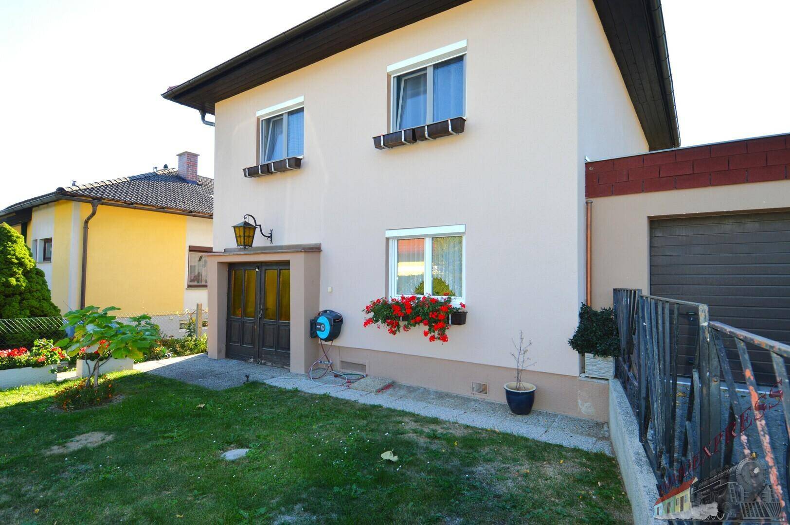 Ansicht der Hausfassade mit Eingangstür, Fenstern und einer Garageneinfahrt auf der rechten Seite.