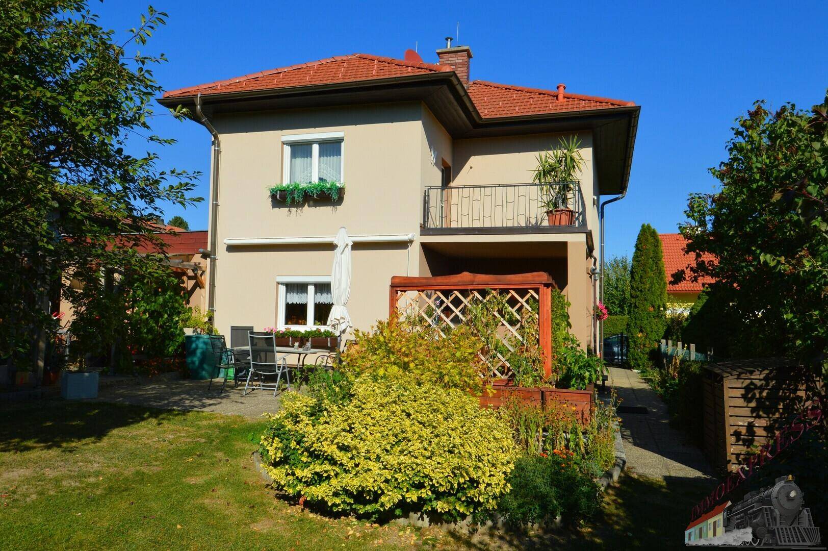Rückseite des Hauses mit einer möblierten Terrasse, gepflegtem Garten und einem kleinen Balkon.