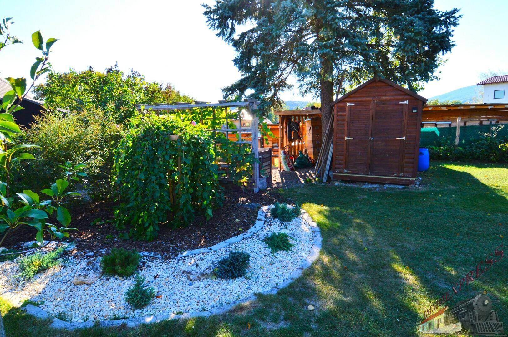 Gepflegter Gartenbereich mit Rasen, Zierbeeten und einem Gartenhaus unter blauem Himmel.