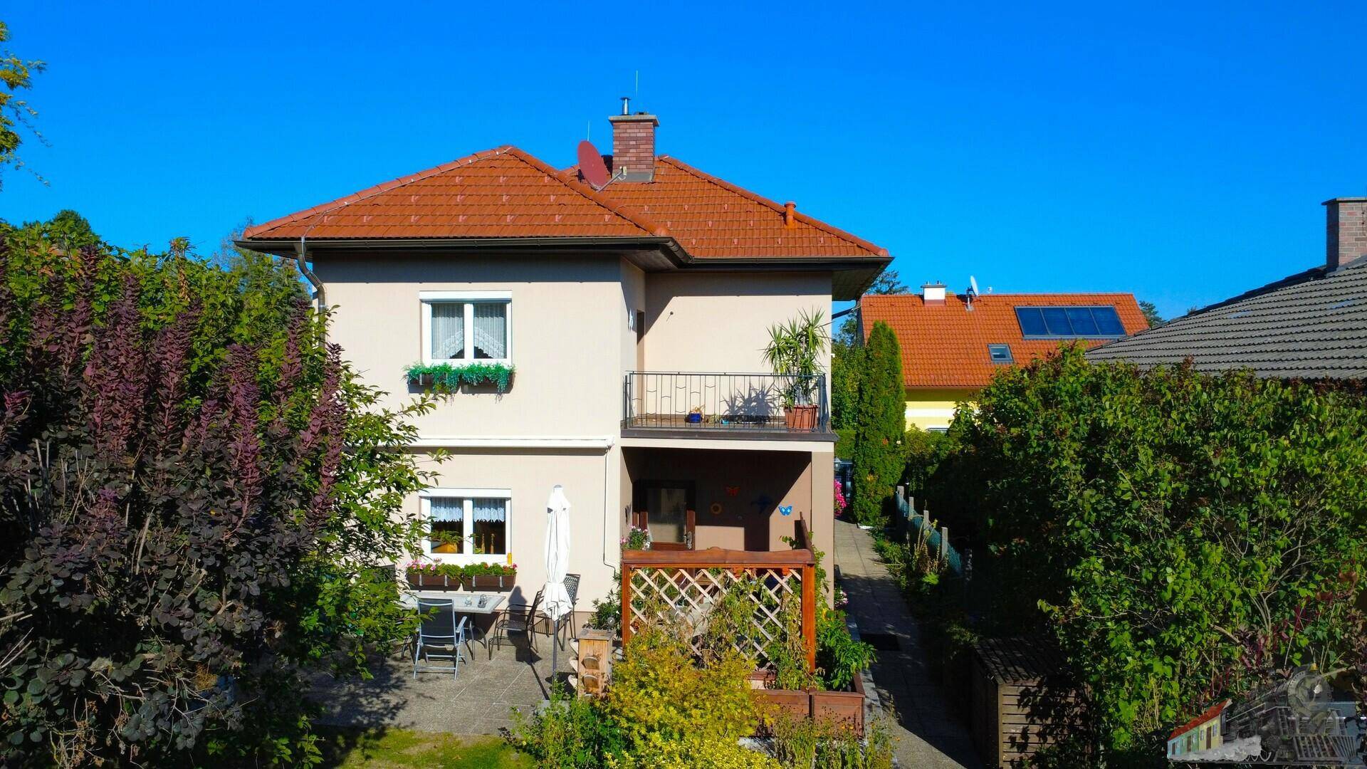 Ansicht des Hauses von hinten mit Terrasse, Balkon und gepflegtem Gartenbereich im Sonnenlicht.