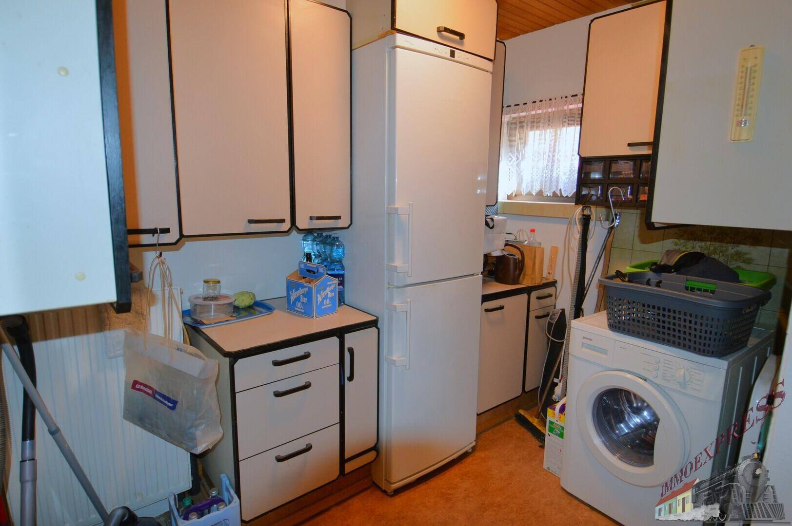 Hauswirtschaftsraum im Keller mit Waschmaschine, Kühlschrank und einfachen Schränken.