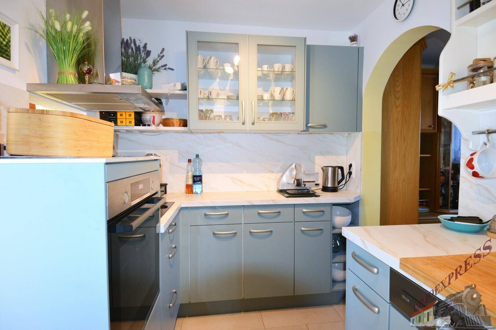 Moderne Küche in Hellblau mit Einbaugeräten, Dunstabzugshaube und Arbeitsplatten in Marmoroptik.
