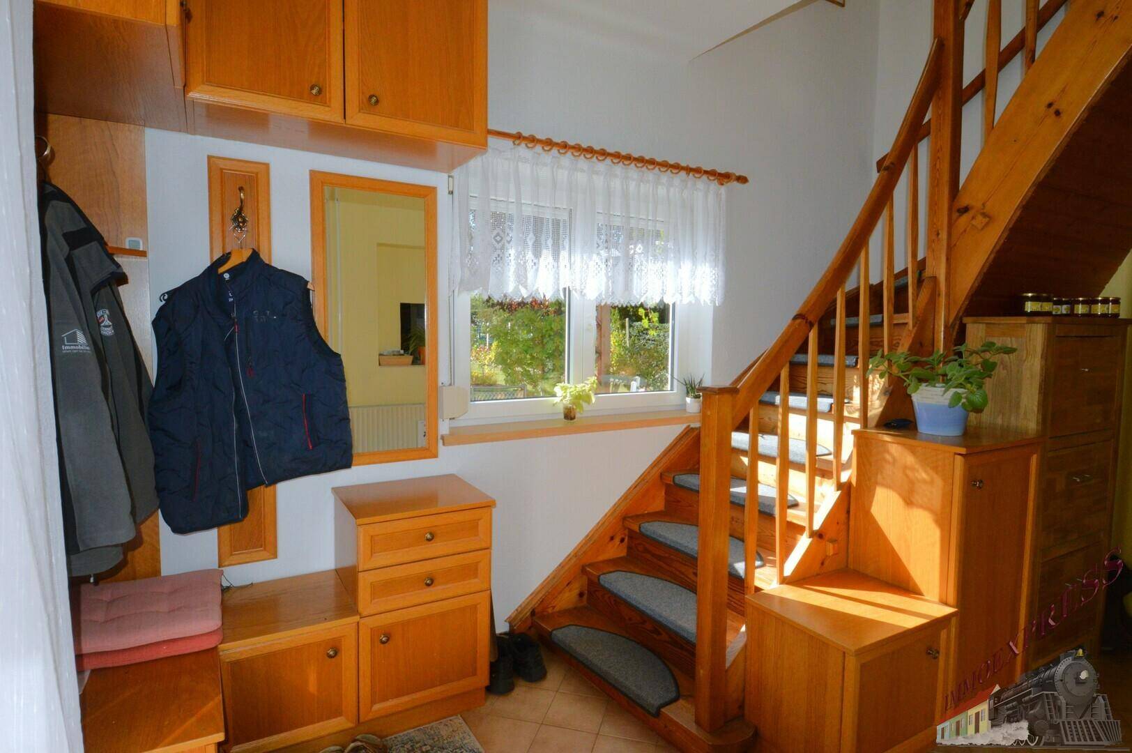 Heller Eingangsbereich mit Holztreppe, Garderobe und Fenster, das Tageslicht hereinlässt.