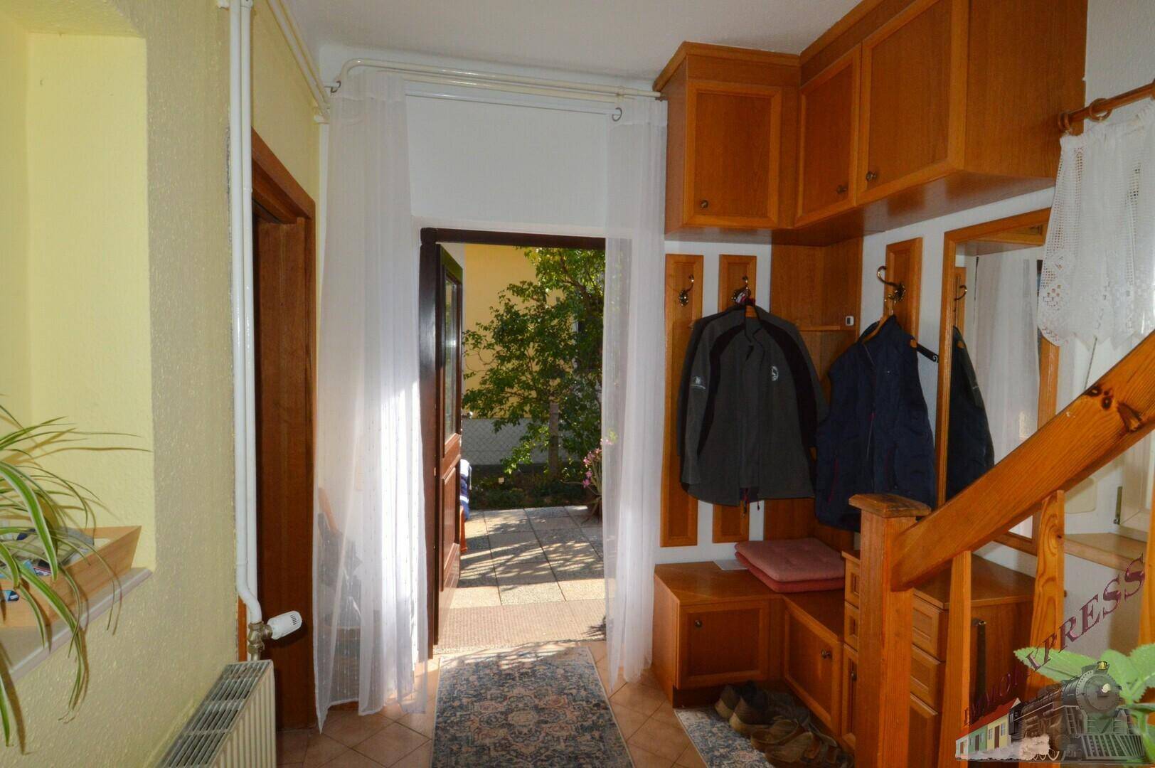 Eingangsbereich mit Garderobe, Holzmöbeln und Blick ins Grüne durch die offene Tür.