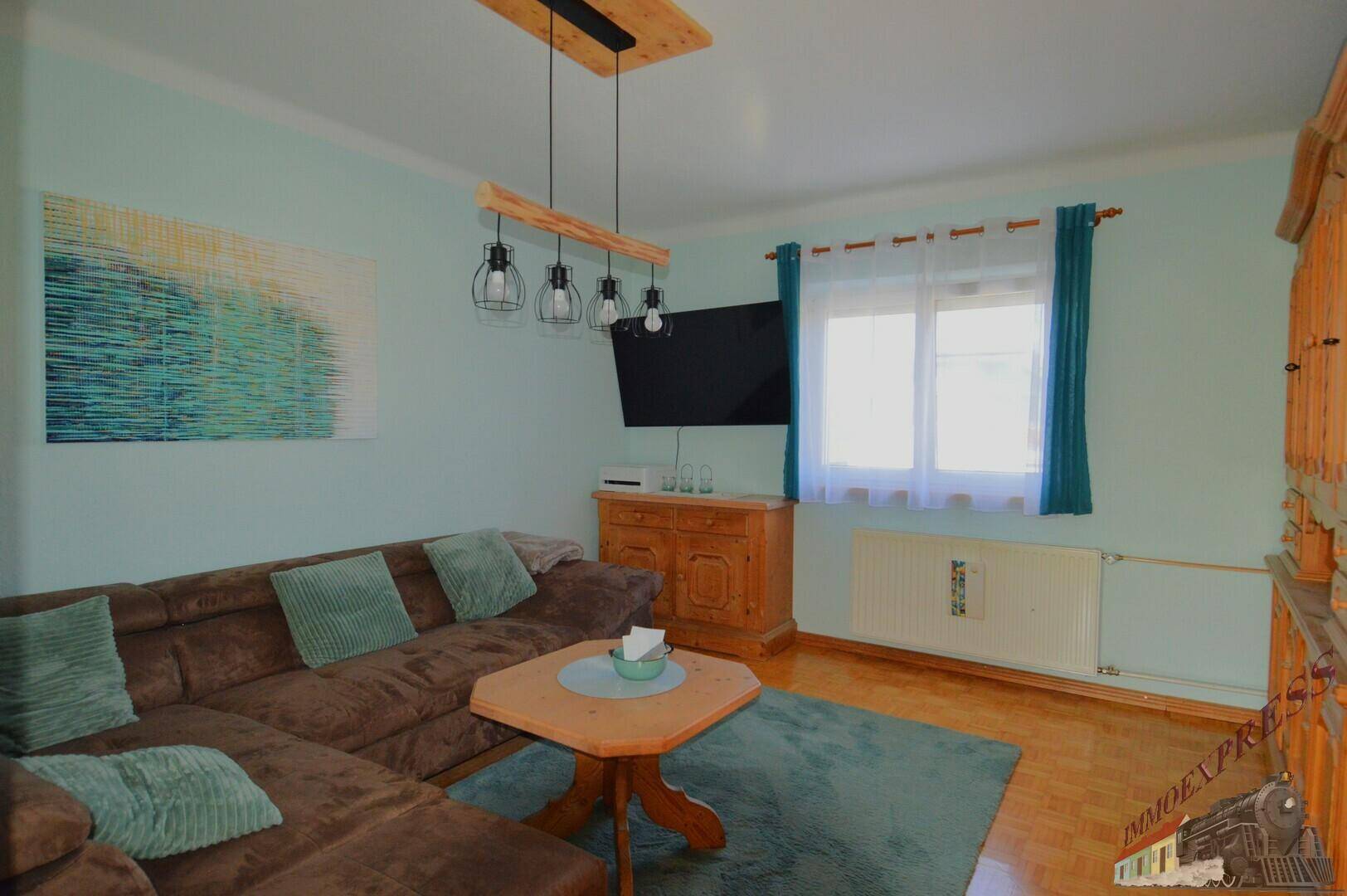 Gemütliches Wohnzimmer mit Ecksofa, Holzboden und modernem Deckenlicht, hell und einladend.
