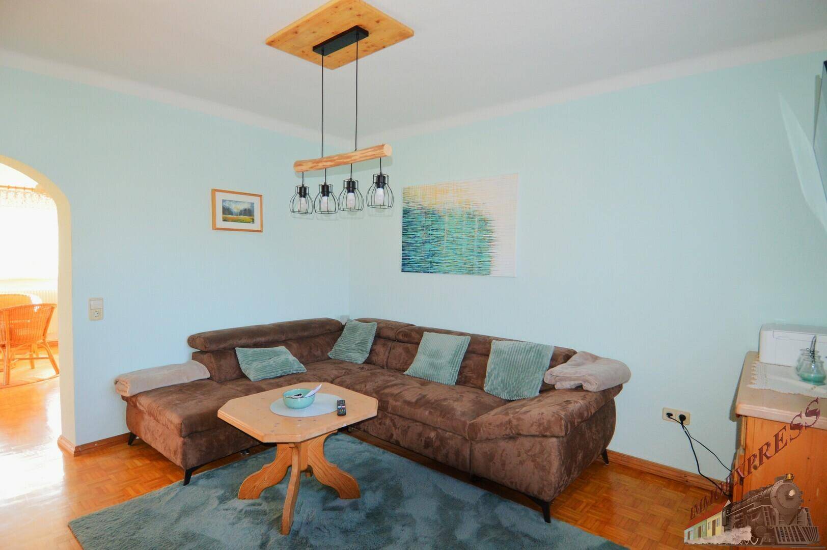 Heller Wohnbereich mit bequemer Couch, Holzboden und Blick in den Essbereich durch einen Bogen.