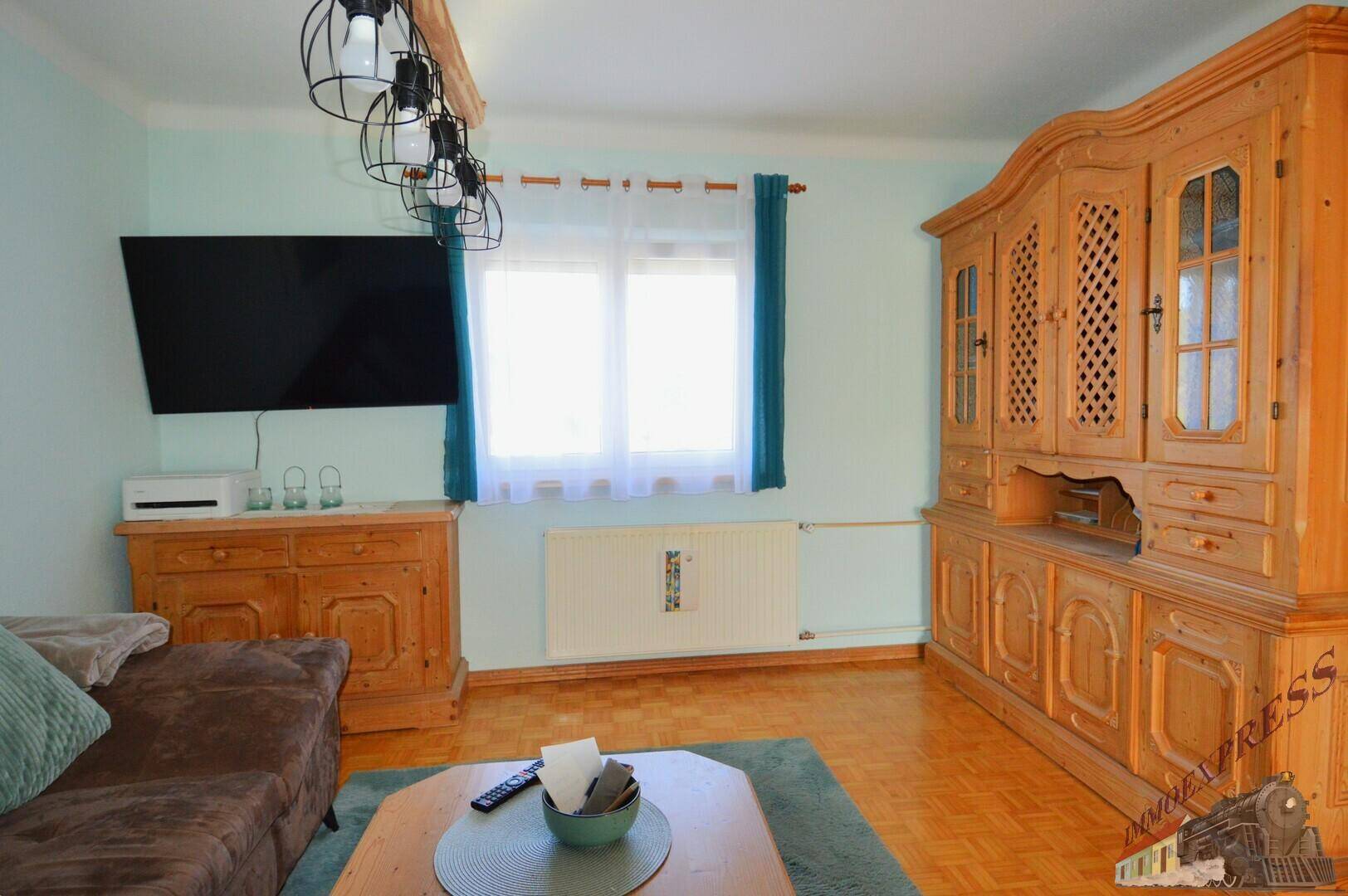 Wohnzimmer mit großem Holzschrank, Fernseher und hellem Fenster, traditionell eingerichtet.