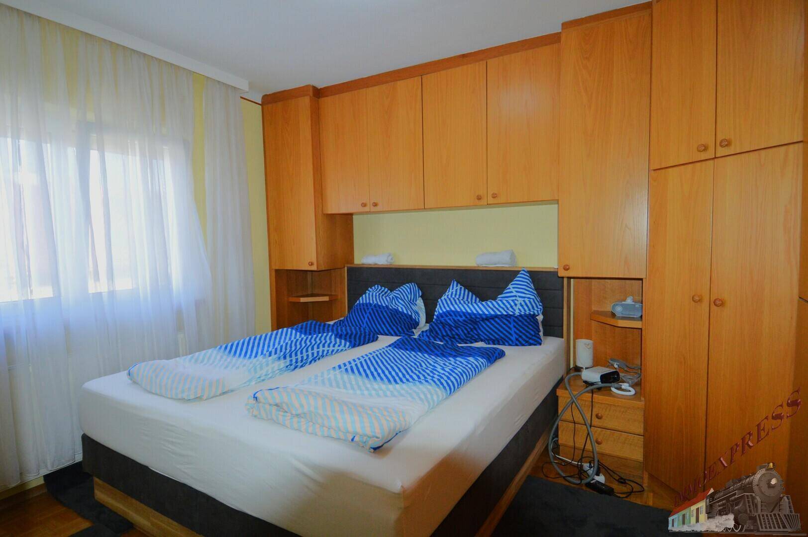 Schlafzimmer mit Einbauschränken, Doppelbett und hellem Fenster, funktional und ordentlich.
