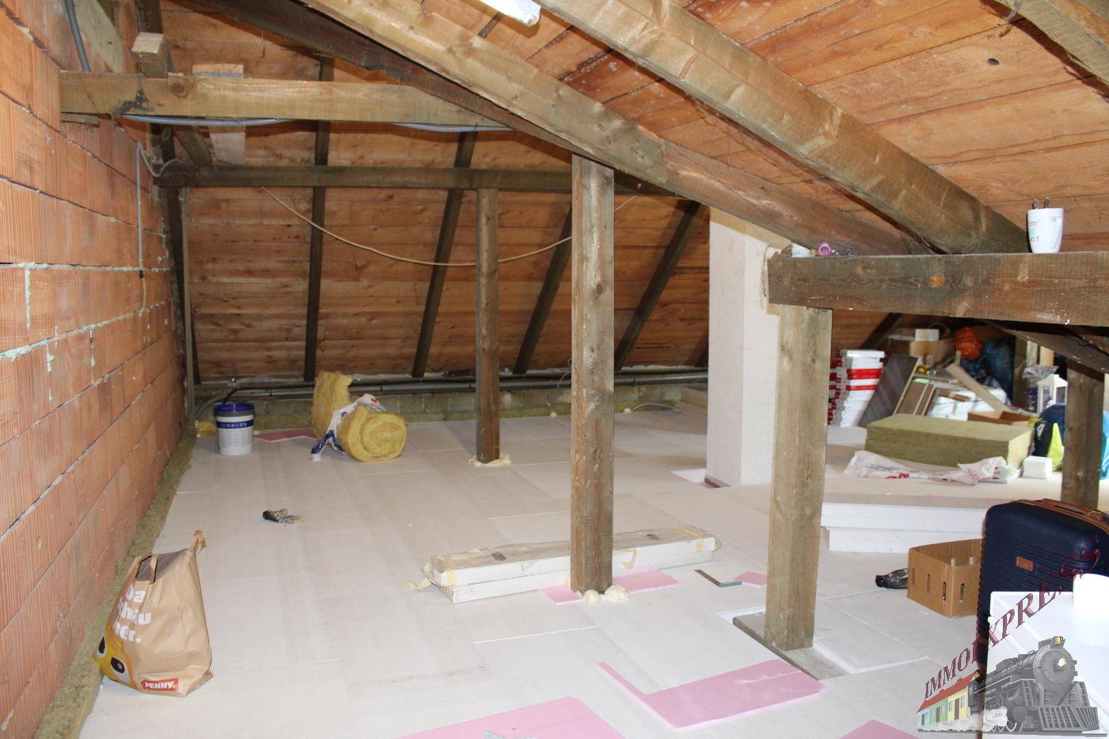 Unfertiger Dachboden mit sichtbaren Holzbalken und Dämmmaterial, bereit für den Ausbau.