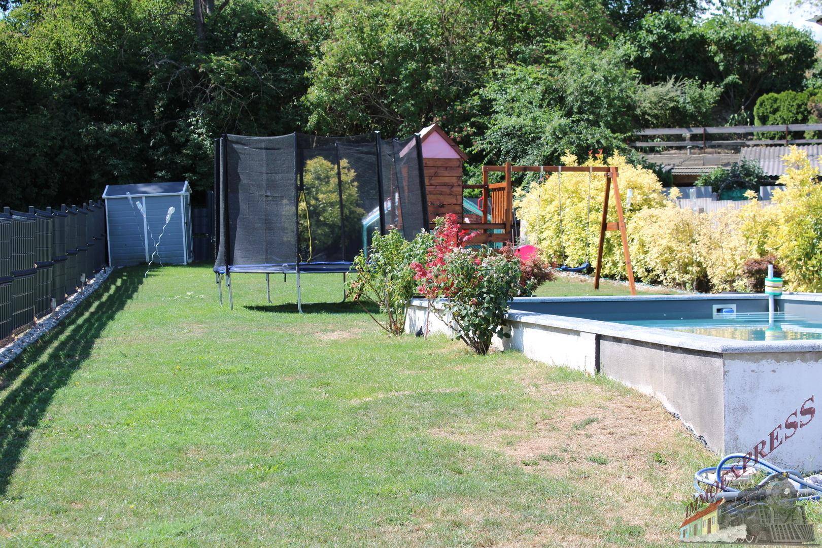 Gartenbereich mit Pool, Spielplatz, Trampolin und umgebender Vegetation.