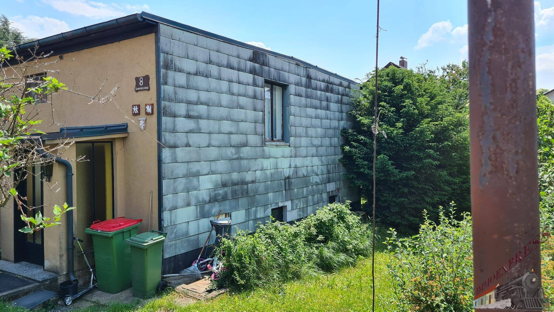 Seitenansicht des Hauses mit Eingangsbereich und einer Fassade aus Schieferplatten.