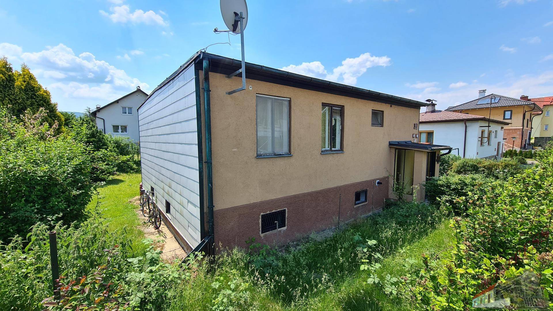 Seitenansicht des Hauses mit beiger Fassade, umgeben von üppiger, grüner Vegetation.