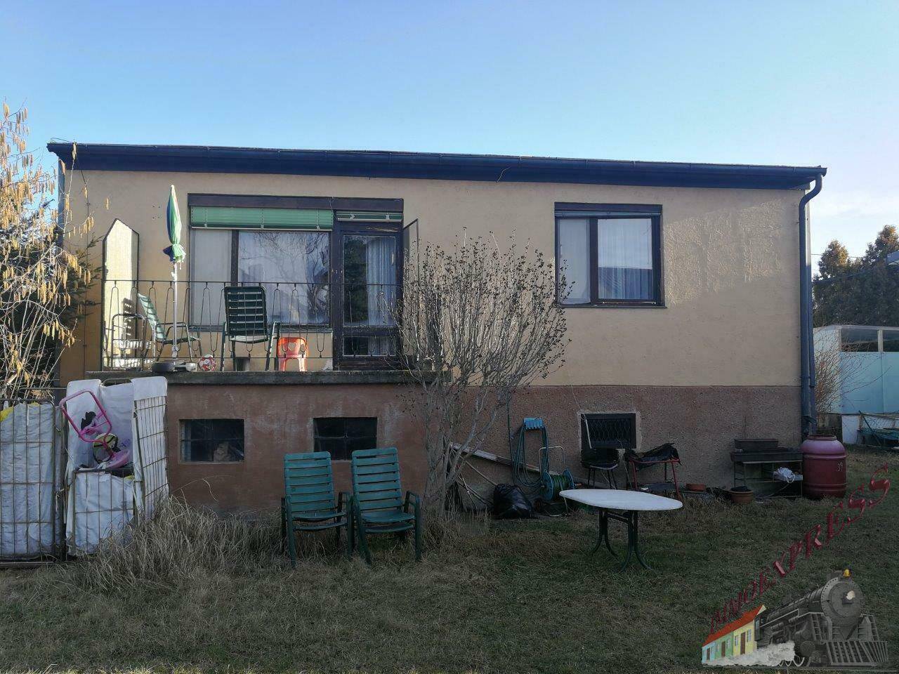 Rückseite des Hauses mit einem kleinen Balkon und einem Gartenbereich, der Pflege benötigt.