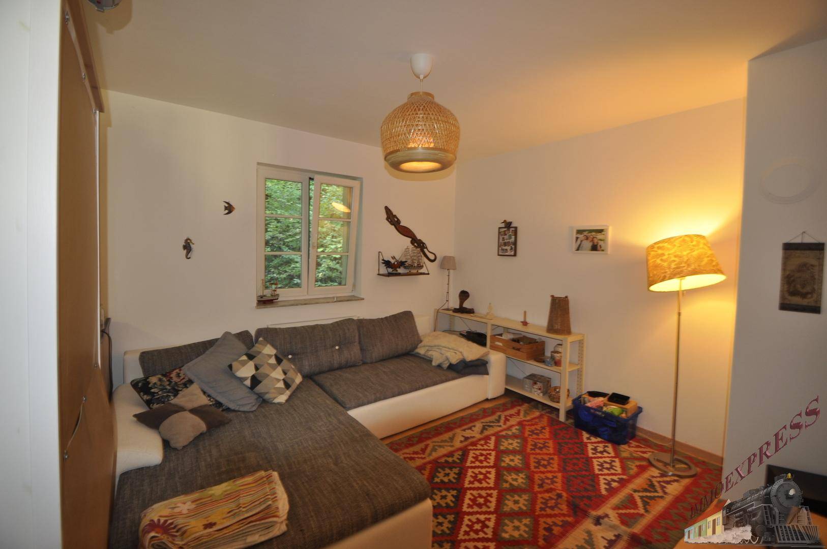 Gemütliches Wohnzimmer mit großem Sofa, farbenfrohem Teppich und Blick ins Grüne.