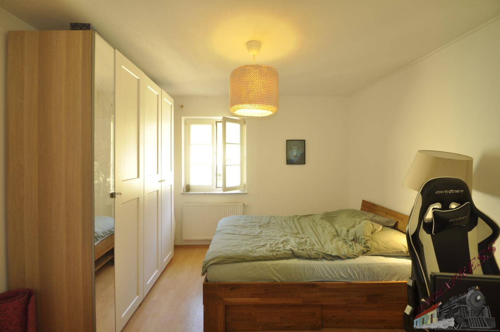 Schlafzimmer mit Holzbett, weißem Kleiderschrank und hellem Fenster.