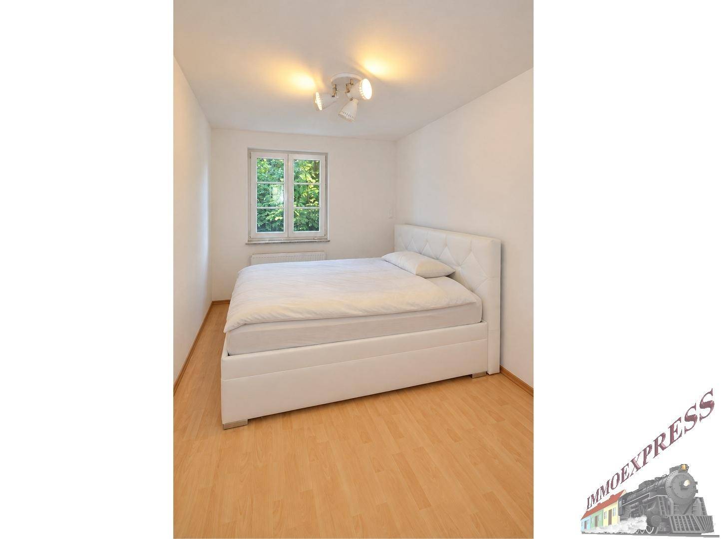 Schlafzimmer mit modernem, weiß gepolstertem Bett und Fenster.