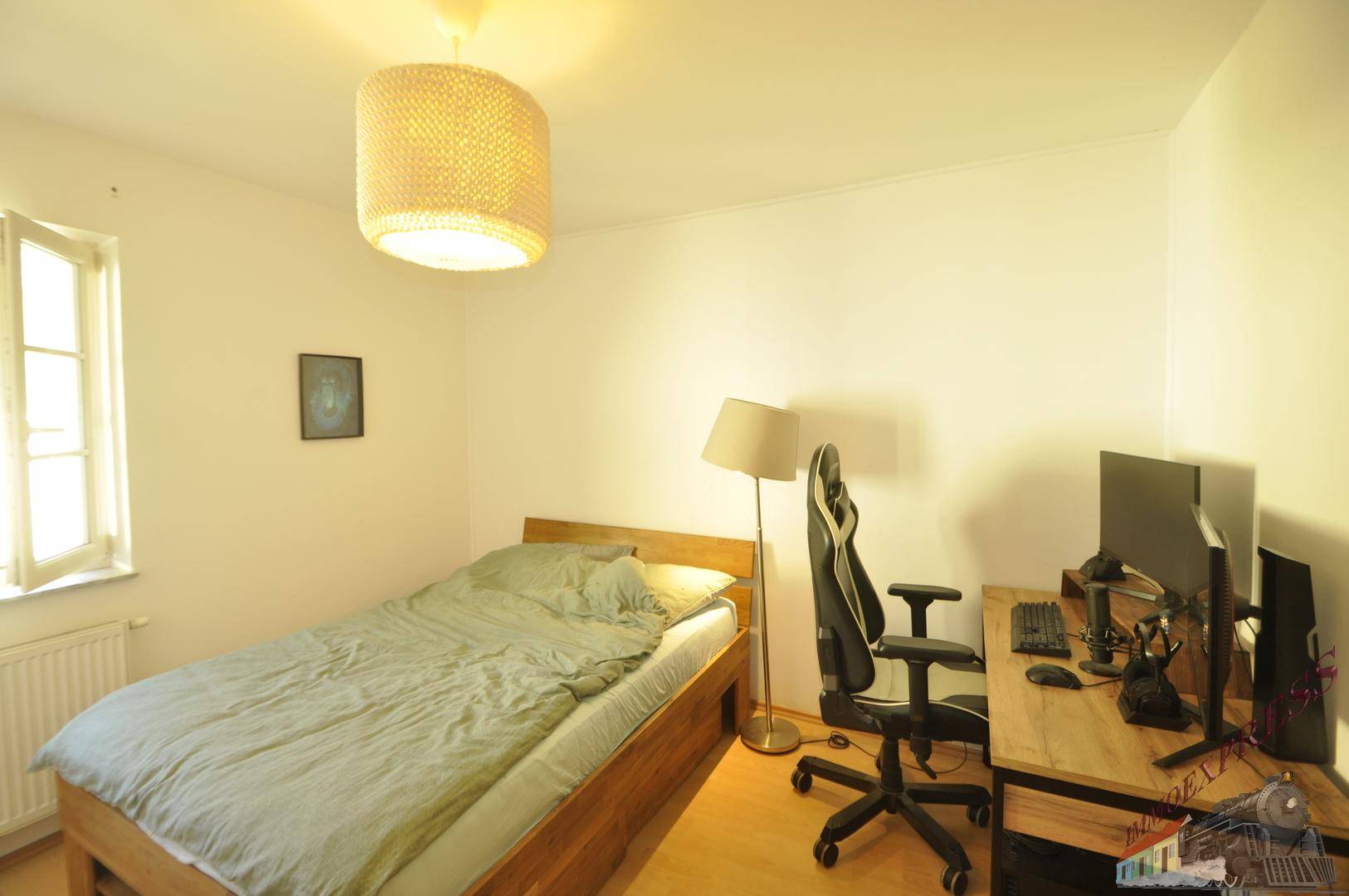 Jugendzimmer mit Einzelbett, Schreibtisch und Computer-Setup am Fenster.
