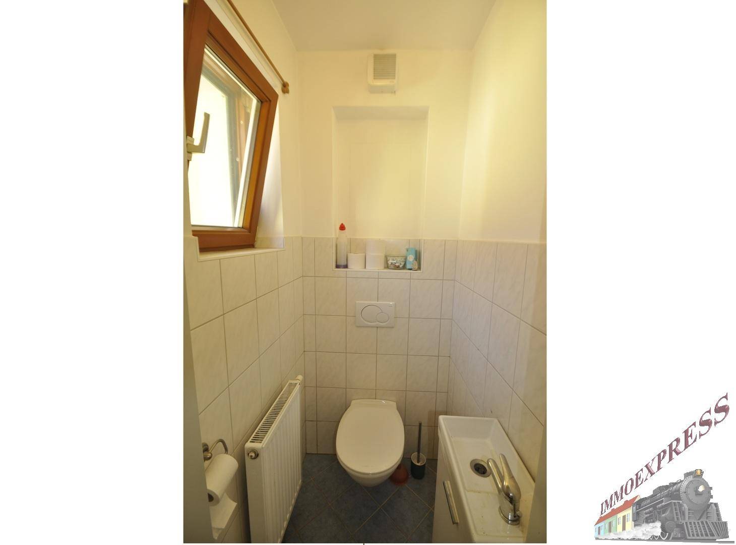 Separates WC mit Toilette, kleinem Waschbecken und Fenster.