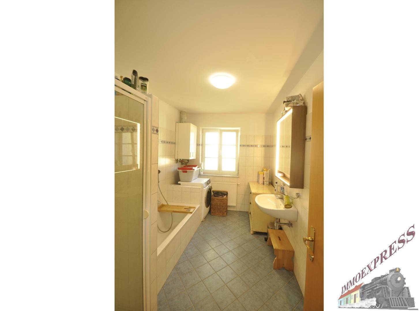 Badezimmer mit Badewanne, Dusche, Waschbecken, Waschmaschine und Fenster.