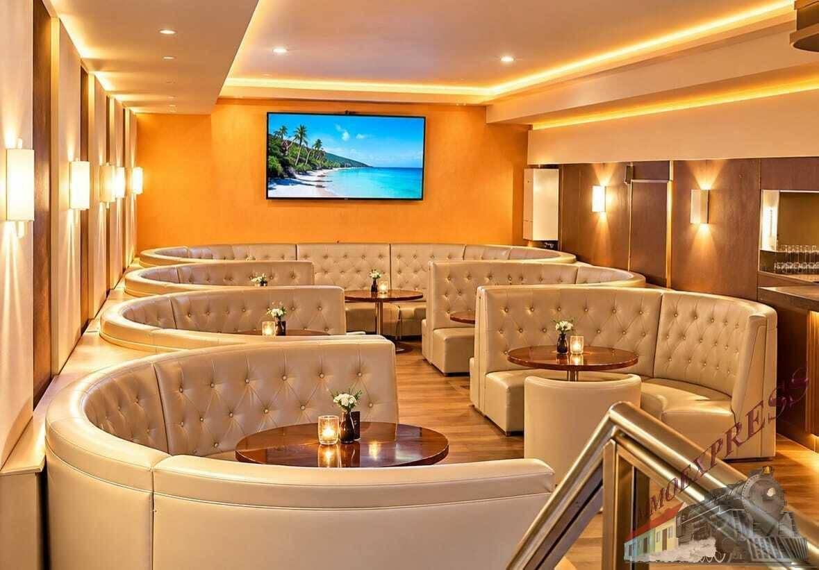 Elegante Lounge mit geschwungenen Sitzbänken, kleinen Tischen und einem großen Flachbildschirm für Unterhaltung.