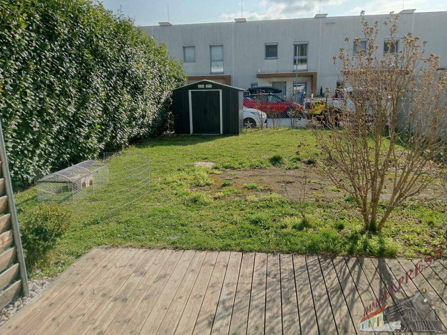 Gartenbereich mit Holzterrasse, Rasenfläche und einem kleinen Geräteschuppen im Hintergrund.