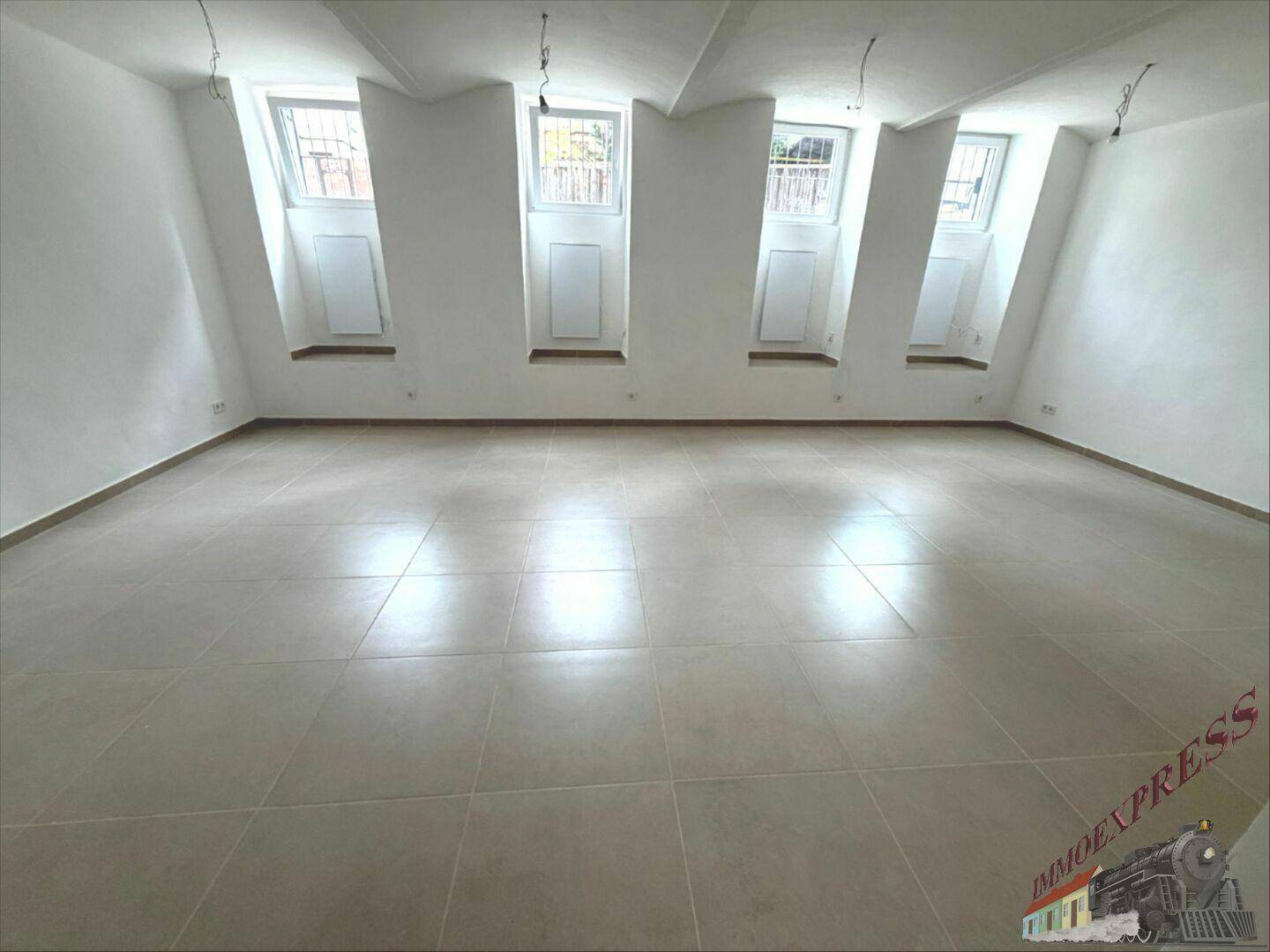 Großer, leerer Raum mit schrägen Wänden und mehreren Fenstern, die viel Tageslicht hereinlassen.