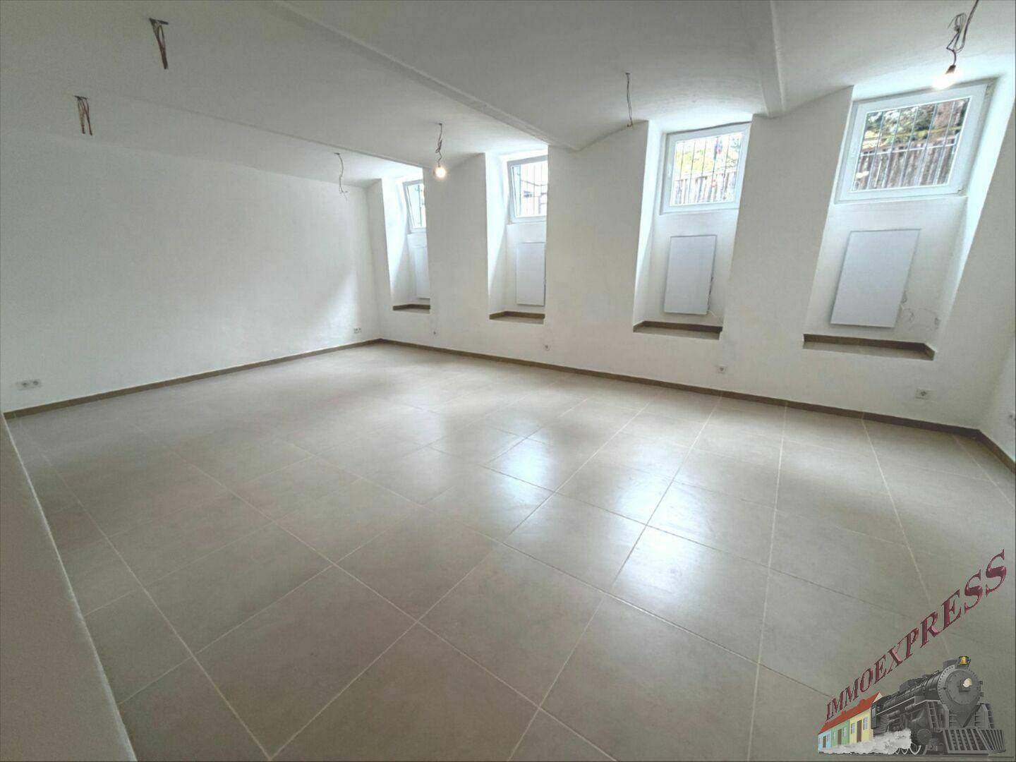 Geräumiger Wohnbereich mit schrägen Wänden, Fliesenboden und mehreren Fenstern für natürliche Belichtung.