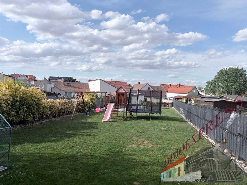 Geräumiger Garten mit Spielgeräten, Trampolin und umzäunter Rasenfläche.