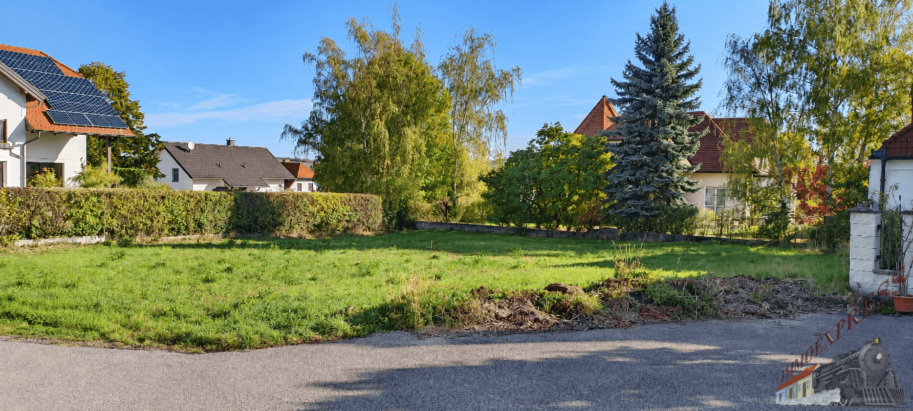 Unbebautes Grundstück mit gepflegter Rasenfläche, umgeben von Hecken und Wohnhäusern.