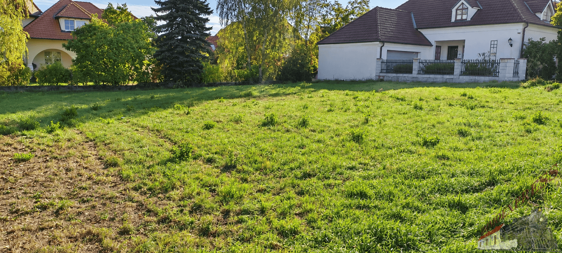 Sonniges Grundstück mit Grasfläche und angrenzenden Wohnhäusern unter blauem Himmel.