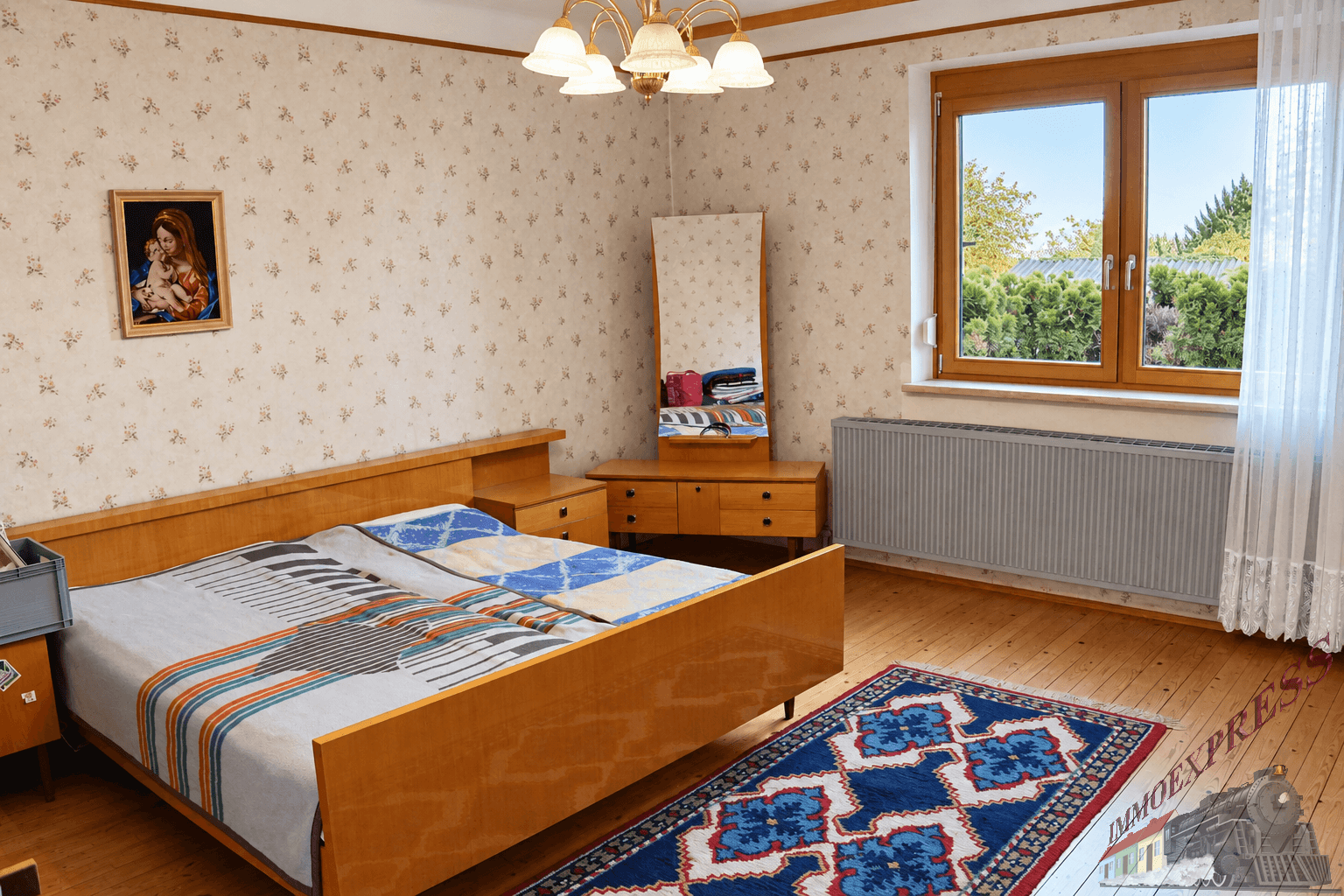Schlafzimmer mit Doppelbett, floraler Tapete und Fenster mit Blick ins Grüne.